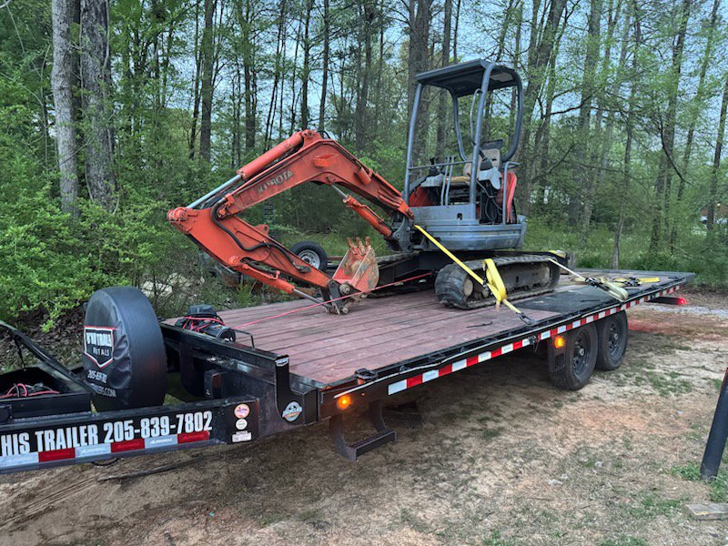 An orange excavator secured on a flatbed trailer for equipment transport by B'ham Trailer Rentals in Alabaster, AL.