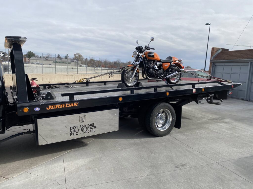 An orange motorcycle being transported on a flatbed tow truck by Black Mamba Towing & Recovery Llc in Aurora, CO.