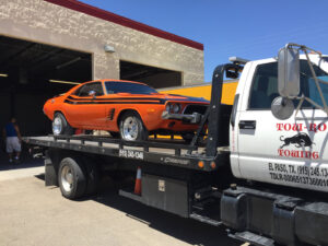 An orange vintage muscle car being transported on a flatbed tow truck by Tow-Ro Towing in El Paso, TX.