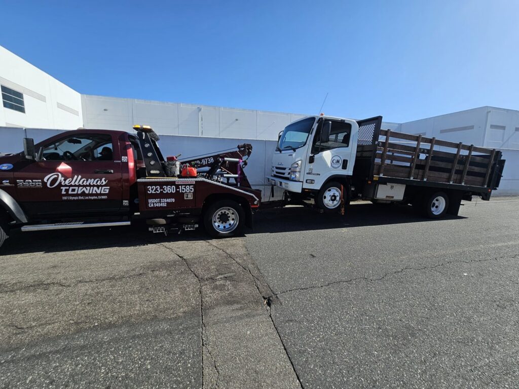 An Orellanas Towing truck actively towing a white flatbed truck in Los Angeles, CA.