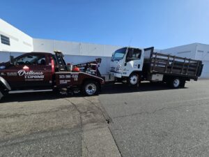 An Orellanas Towing truck actively towing a white flatbed truck in Los Angeles, CA.