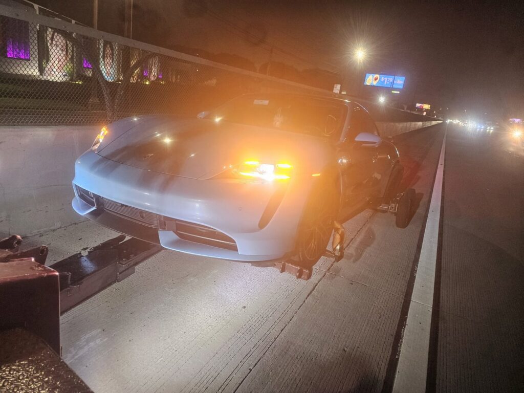 An Orellanas Towing truck towing a white Porsche Taycan on a highway at night in Los Angeles, CA.