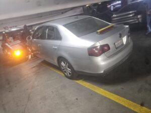 An Orellanas Towing truck actively towing a silver Volkswagen Jetta in a parking garage in Los Angeles, CA.