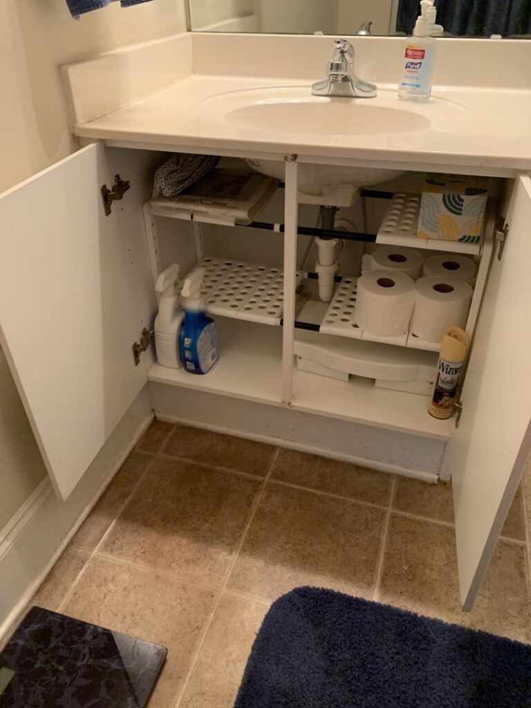 An organized bathroom cabinet with cleaning supplies and neatly stacked toilet paper by SetApart Home Concierge in Greenville, SC.