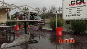 An outdoor area with significant standing water and debris, indicating a water damage event, with a COIT Cleaning and Restoration truck in Indianapolis, IN on site