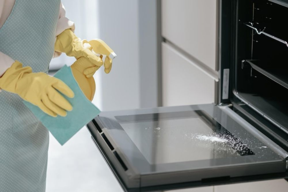 Hands in yellow gloves spray and wipe the interior of an oven for Glory Cleaning Service in Irvine, CA.