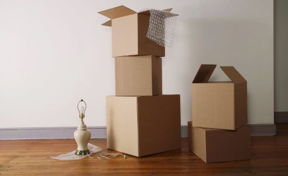 Stacked cardboard moving boxes and a lamp in an empty room, ready for transport by Emanuel Movers, Inc. in Houston, TX