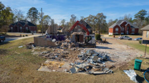 A residential house undergoing partial demolition, with an excavator visible in the background, by Nuckles Services in Birmingham, AL