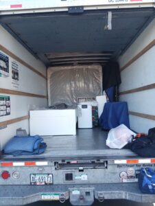 The back of a moving truck partially loaded with a mattress, boxes, and moving blankets by Rough Çutt Movers in San Diego, CA.