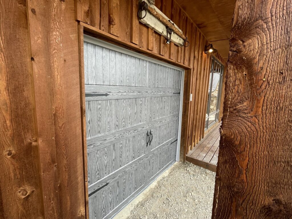 A partially open grey wood-grain style garage door with decorative hardware installed by Elite Garage Door Service & Repair in Billings, MT.