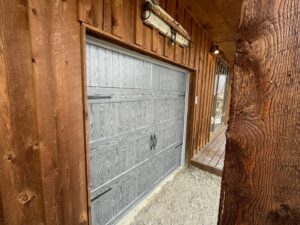 A partially open grey wood-grain style garage door with decorative hardware installed by Elite Garage Door Service & Repair in Billings, MT.