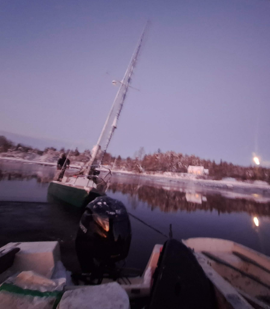 Downeast Marine Towing, LLC crew recovering a partially submerged sailboat in Eastport, ME during dusk.