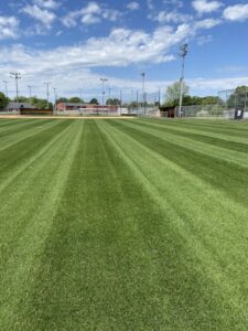 A perfectly mowed baseball field with distinct stripes, showcasing professional lawn care by The Otherside Lawn Solutions in Ankeny, IA.