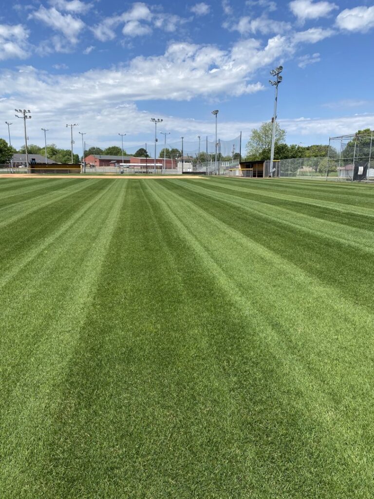 A perfectly mowed baseball field with distinct stripes, showcasing professional lawn care by The Otherside Lawn Solutions in Ankeny, IA.