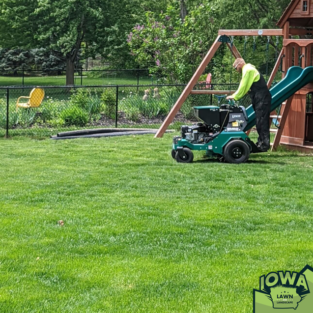A person operating a walk-behind aerator on a residential lawn for Iowa Lawn and Landscape LLC in Des Moines, IA.