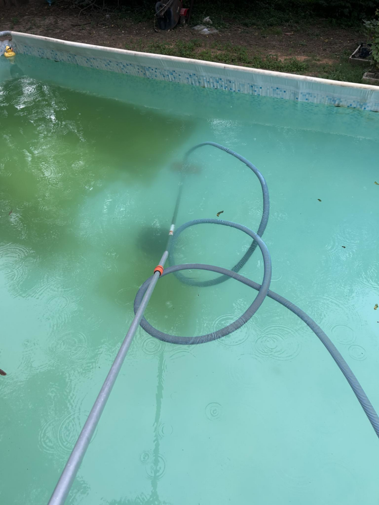 A person actively cleaning an algae-filled green pool with a vacuum pole, demonstrating work by Pips Pool Service in Enid, OK.