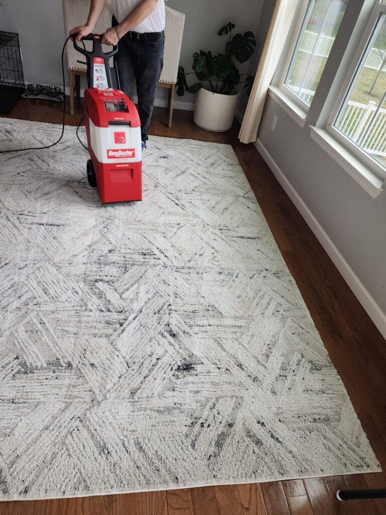 A person using a Rug Doctor machine to professionally clean a large area rug in a home by Harsh's Cleaning Services LLC in Canton, OH.