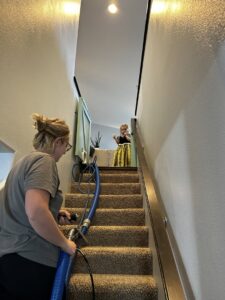 A professional from FM Cleaning cleaning carpeted stairs with a specialized wand in a home in West Fargo, ND.