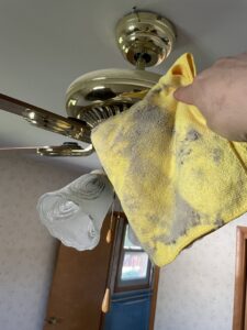 A hand holding a dirty cloth cleaning a dusty ceiling fan, demonstrating deep cleaning by Deep Cleaning Service in Frederick, MD.