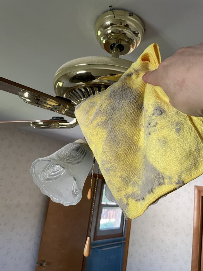 A hand holding a dirty cloth cleaning a dusty ceiling fan, demonstrating deep cleaning by Deep Cleaning Service in Frederick, MD.