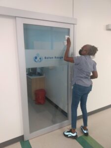 A cleaner wiping down a glass door, demonstrating window and glass cleaning by Janice Janitorial LLC in Baton Rouge, LA.