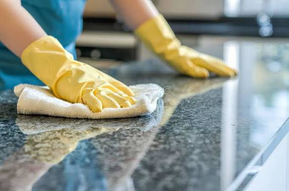 A person wearing yellow gloves cleaning a granite countertop with a white cloth for Deep Cleaning Service in Frederick, MD.
