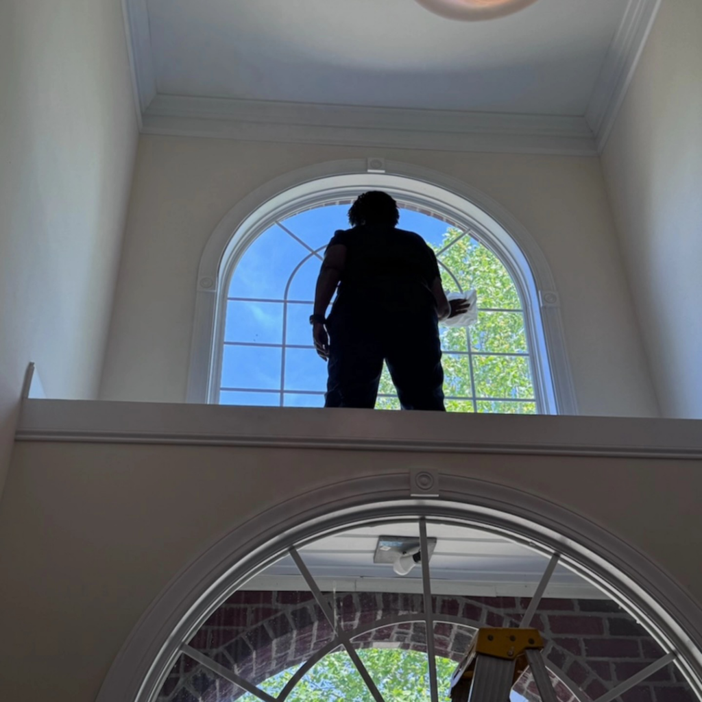 A cleaner from Impeccable Cleaning Service meticulously cleaning a high arched window in Columbia, SC.
