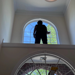A cleaner from Impeccable Cleaning Service meticulously cleaning a high arched window in Columbia, SC.