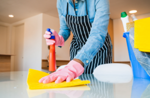 A professional house cleaner wiping down a kitchen counter with spray and a cloth for Price Cleaning Services Omaha in Council Bluffs, IA.