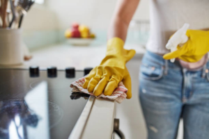 A person wearing yellow gloves cleaning a kitchen stovetop with a cloth and spray bottle for Mike's Cleaning Crew in Cincinnati, OH