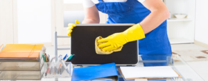 A professional cleaner from Klean Living in Lawson, Dallas, TX, meticulously wiping a laptop screen on a desk.