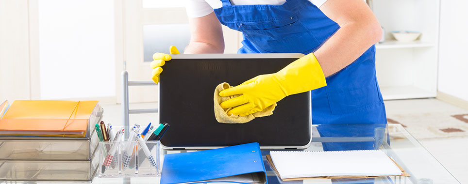 A professional cleaner from Klean Living in Lawson, Dallas, TX, meticulously wiping a laptop screen on a desk.