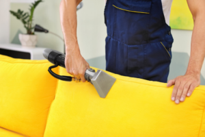 A person cleaning a yellow sofa's upholstery with a specialized tool, provided by Chinook Services Silver Lake in Everett, WA