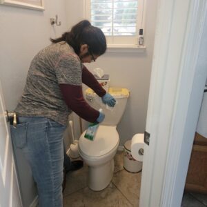 A professional cleaner from Dust Bunnies Cleaning Services in Bakersfield, CA, meticulously cleaning a toilet.
