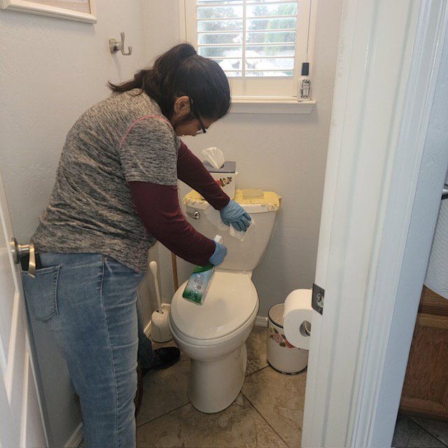 A professional cleaner from Dust Bunnies Cleaning Services in Bakersfield, CA, meticulously cleaning a toilet.