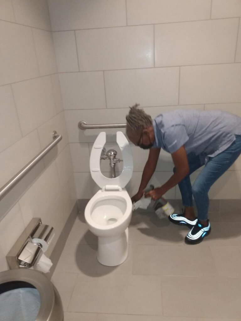 A professional cleaner meticulously cleaning a toilet, a service offered by Janice Janitorial LLC in Baton Rouge, LA.