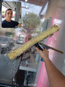 A person's hand using a squeegee to clean a window, demonstrating window cleaning services by Gavin's Cutting Edge in Moscow, ID.
