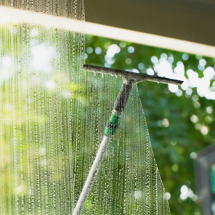 A person cleaning a window with a squeegee, showing professional window cleaning by Phoenix Move Out House Cleaning Pros in Chandler, AZ
