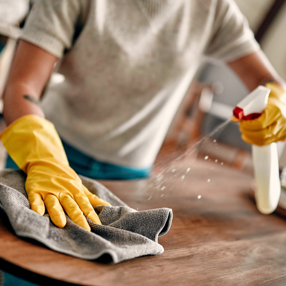 A person in yellow gloves spraying and wiping a wooden table, showcasing cleaning services by Phoenix Move Out House Cleaning Pros in Chandler, AZ