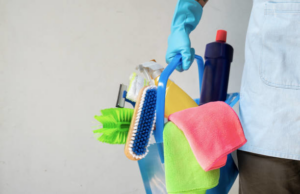 A person wearing a blue glove holding a caddy filled with various cleaning supplies for Infinite Cleaning in Minneapolis, MN.