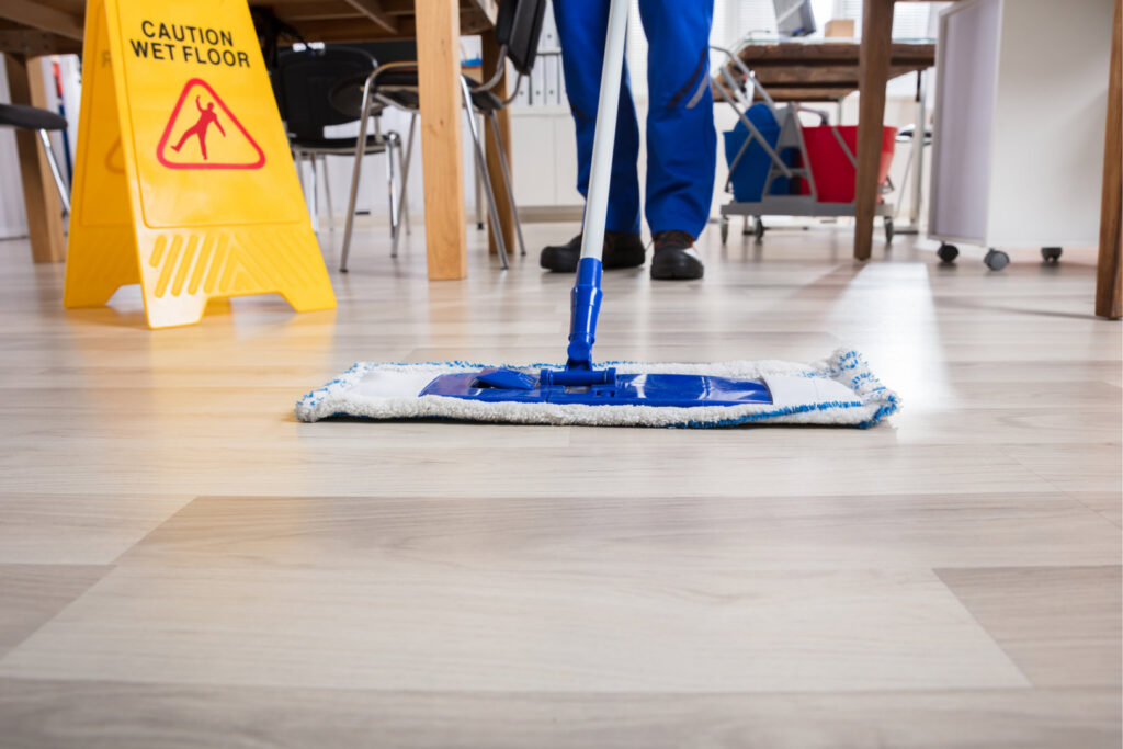 A person mopping a light wood floor with a 'Caution Wet Floor' sign, demonstrating cleaning by Le Fine Cleaning in South Bend, IN.