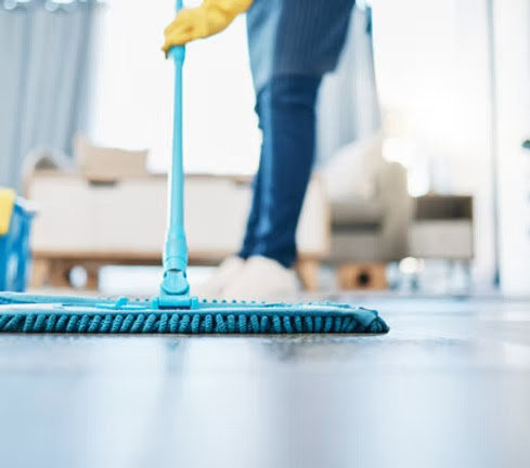 A person wearing yellow gloves mopping a floor with a blue mop, demonstrating house cleaning by MAGA maids in Knoxville, TN.