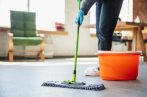 A person wearing gloves mopping a floor with a bucket, demonstrating house cleaning services from Stella's Professional Cleaning LLC in Wilmington, NC.