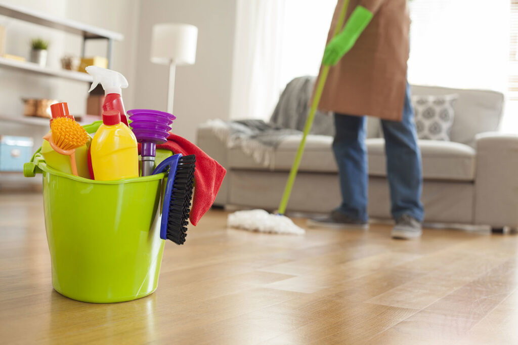 A person mopping a wooden floor in a clean living room, with a bucket of cleaning supplies in the foreground, by Full Circle Commercial Cleaning in Scottsdale, AZ.