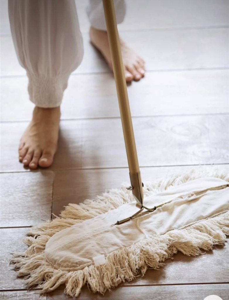 A person mopping a wooden floor with a large mop, demonstrating house cleaning services by ECS Tulsa in Tulsa, OK.