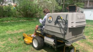 A person operating a riding lawn mower, performing lawn care services for Steele Lawns in Portland, ME.