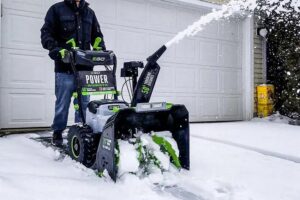 A person operating an EGO Power+ snow blower to clear snow from a residential driveway for NetZero Property Services in Ann Arbor, MI.