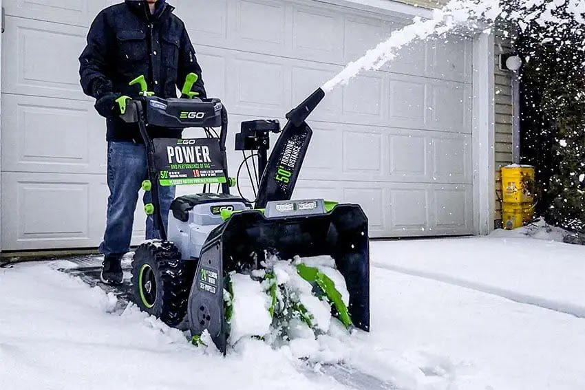 A person operating an EGO Power+ snow blower to clear snow from a residential driveway for NetZero Property Services in Ann Arbor, MI.