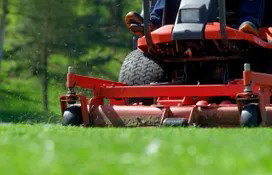 A professional operating a red zero-turn lawn mower, providing expert lawn care for Backcountry Lawn Service in Missoula, MT.