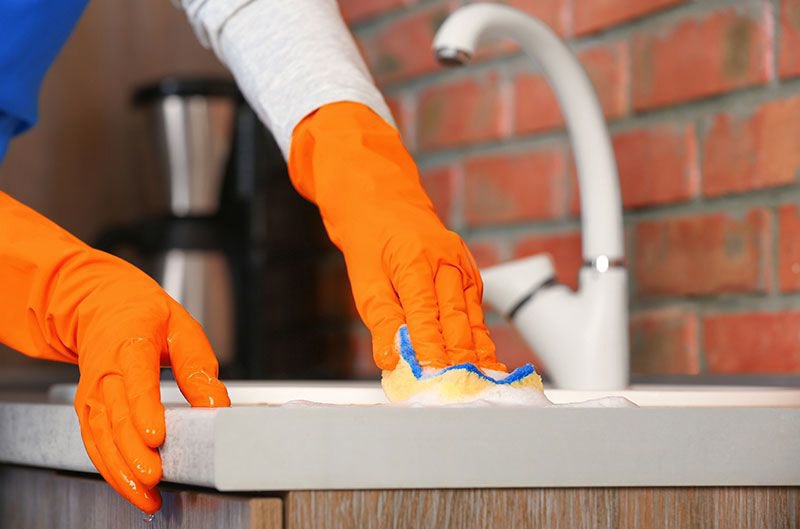 A person wearing orange gloves scrubbing a kitchen counter next to a sink, showcasing house cleaning by Orange Cleaning Services in New Haven, CT